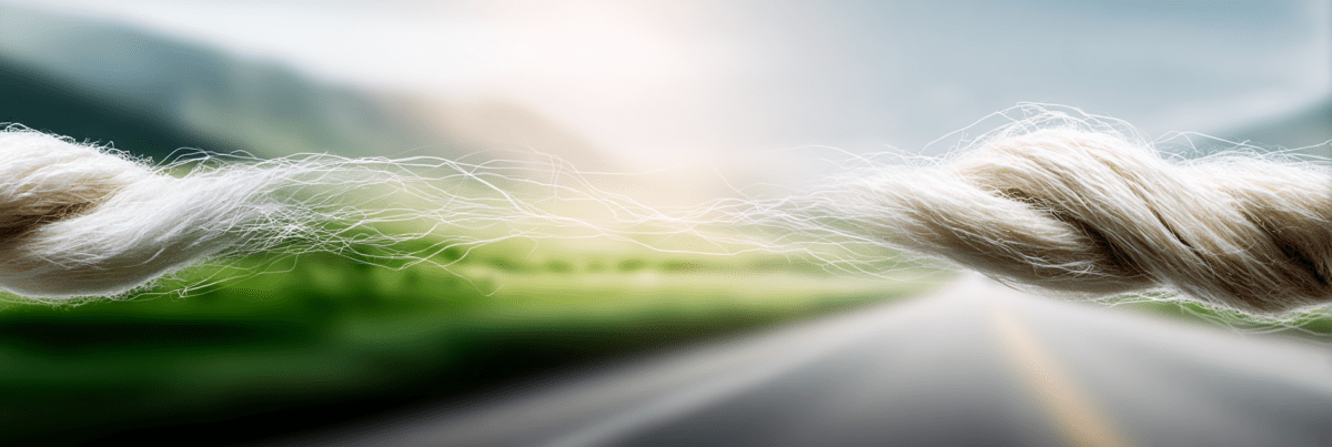 Close-up of a single fiber stretched between two thicker strands, thinning in the middle against a softly blurred landscape and road.