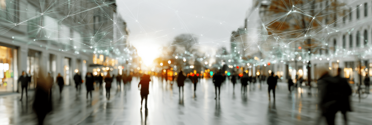 People move through a busy city street beneath faint, interconnected digital networks suspended overhead, illustrating how invisible technologies can become woven into everyday life.